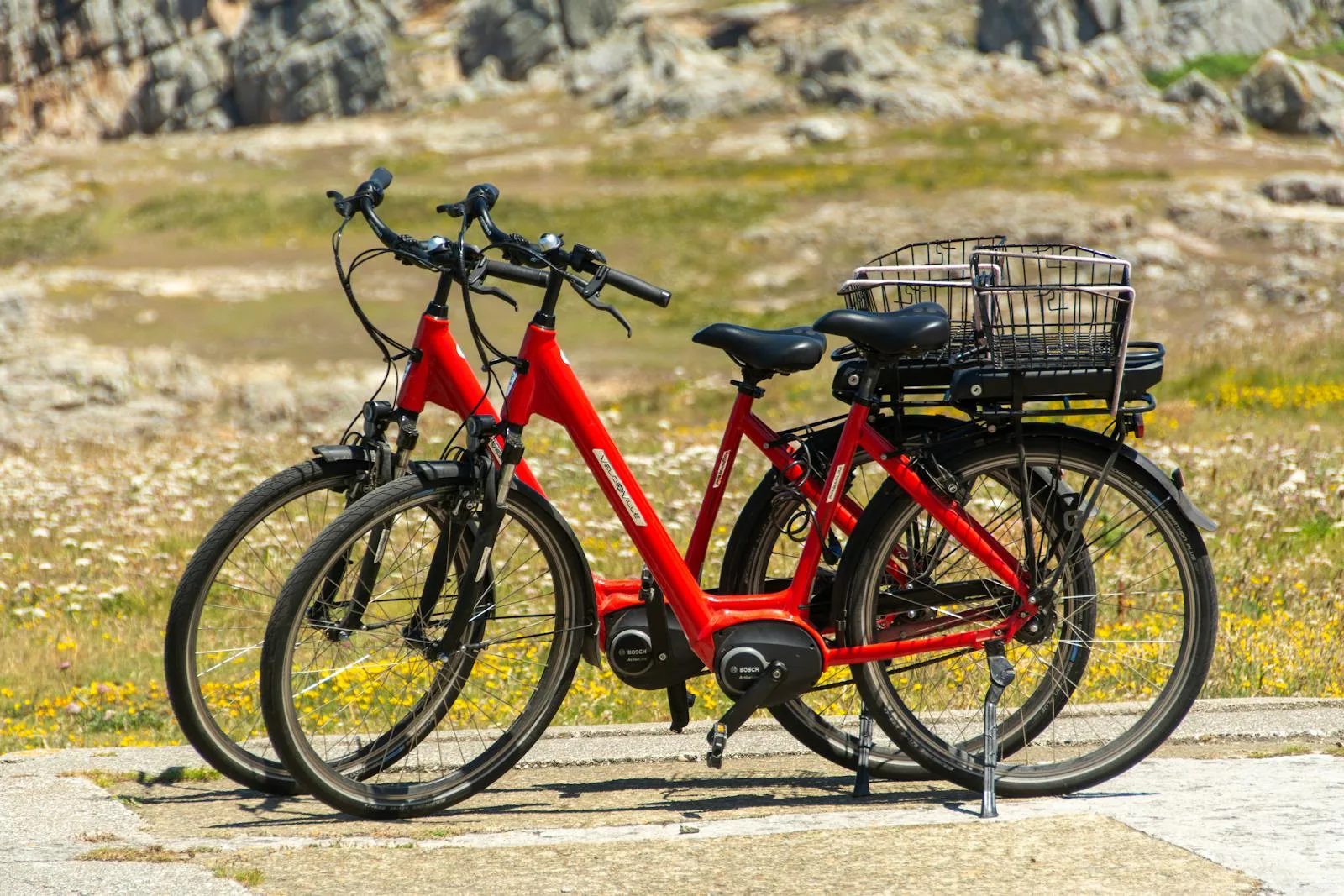 Two red mid-drive e-bikes parked outdoors on a scenic coastal path